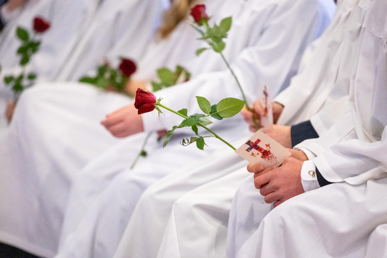 Sittende konfirmanter med røde roser i hendene.
